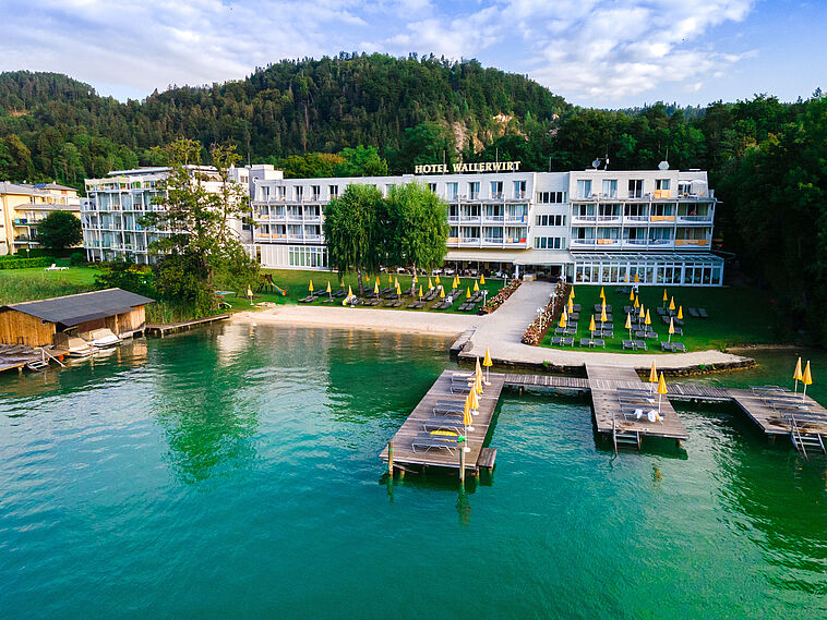 Blick über einen See mit Steg und Hotel im Hintergrund