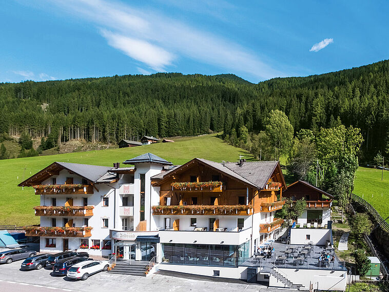 Außenansicht eines südtiroler Hotels mit Wiese und Wald im Hintergrund