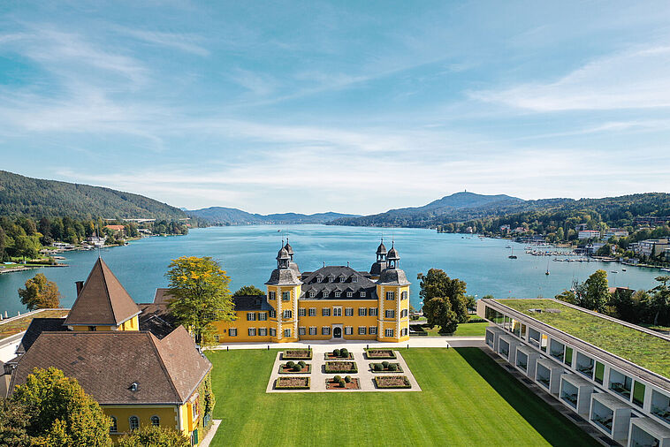 Blick über einen Park auf ein Schloss mit See im Hintergrund