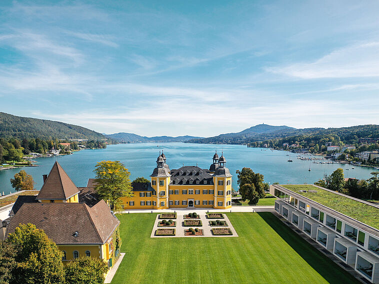 Blick über einen Park auf ein Schloss mit See im Hintergrund